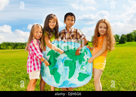 Group of happy kids boys and girls standing and pointing to the globe map depicting diversity concept standing outside  Stock Photo