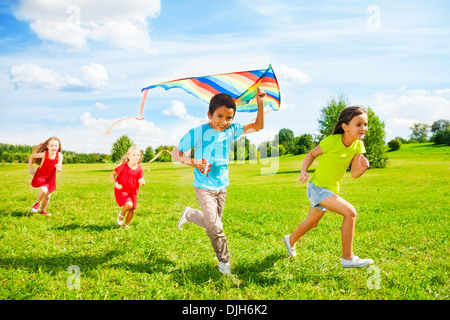 Group of four little kids, boy and girls running with kite in the park on summer day Stock Photo