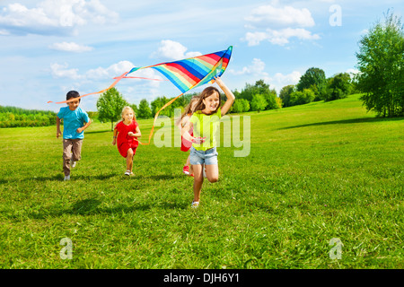 Four little kids running in the park with kite happy and smiling Stock Photo