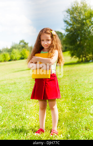 Portrait of beautiful 6 years old girl standing in the park with books on summer day Stock Photo