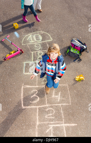 Boy jumping on the hopscotch game drawn on the asphalt looking up Stock Photo