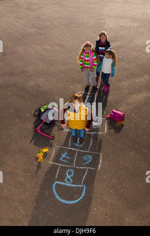 Boy jumping on hopscotch game with mates boys an girls standing by with school bags laying near Stock Photo