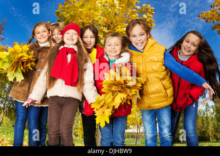 Group of seven kids around 10 years old standing together in the park with autumn yellow maple tree on background Stock Photo