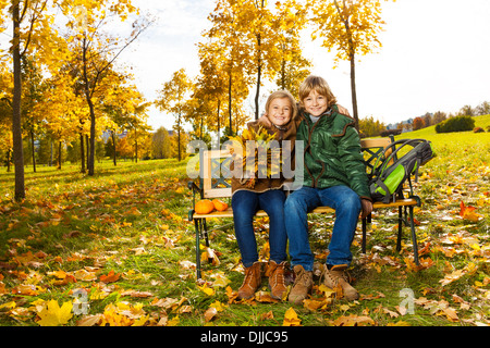 Portrait of two happy blond kids sitting on the bench in autumn park  Stock Photo