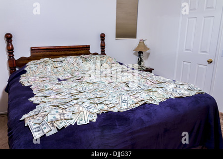 A bed covered in piles of American money. Stock Photo