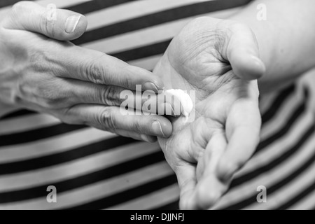 Mature woman spread out skincare cream to her hand, horizon format black and white image Stock Photo