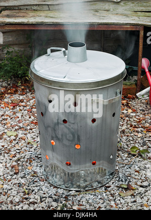 Garden incinerator bin burning garden waste with smoke coming out of the flue Stock Photo