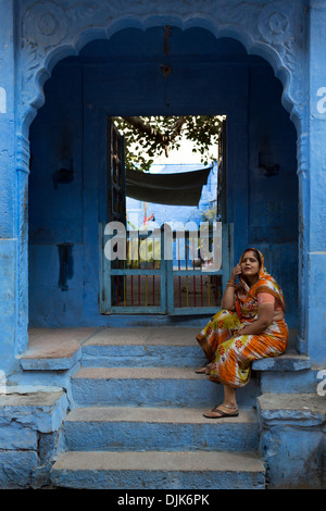 A woman waits sitting on the steps of one of the houses of the city of Jodhpur, the blue city of Rajasthan Stock Photo