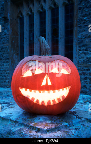 All Hallows Eve. A grinning Halloween Jack o’ Lantern carved from a pumpkin, glowing by candlelight, in an ancient churchyard. England, United Kingdom. Stock Photo
