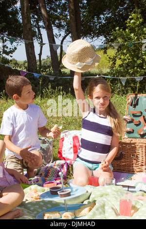 two children sitting around having a picnic, sitting on a blanket eating food in the sunshine with a picnic basket in Somerset, Stock Photo