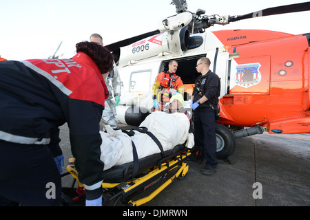 A Coast Guard MH-60 Jayhawk helicopter crew transfers an injured man to a Kodiak City Fire ambulance crew for further transfer to commercial medevac services in Kodiak, Alaska, Nov. 27, 2013. The man injured his head and right eye during a fall aboard the Stock Photo