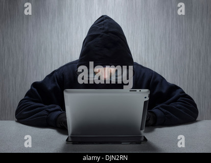 An anonymous hooded male using a tablet computer representing a cyber criminal. Stock Photo