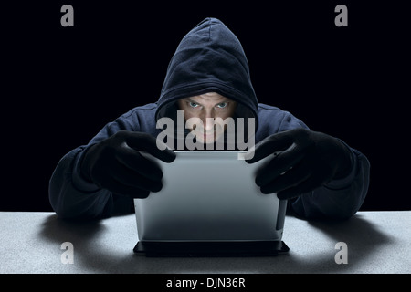 A hooded male representing a cyber criminal, using a tablet computer. Stock Photo
