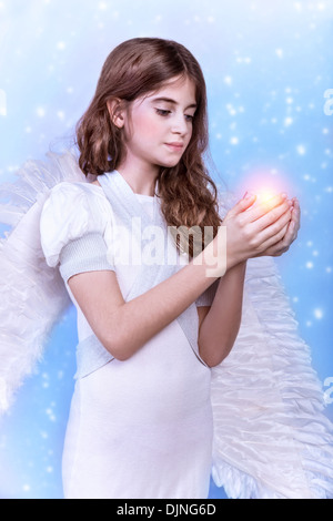 Cute Christmas angel on blue snowy background, adorable girl with candle in hands, religious winter holiday, peace and harmony Stock Photo