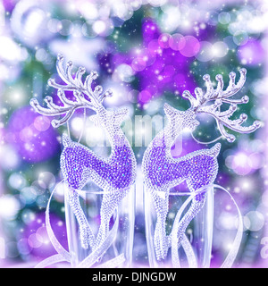 Two glass reindeer ornament on festive blurry background, Christmas tree with purple decoration, wine glasses, New Year party Stock Photo