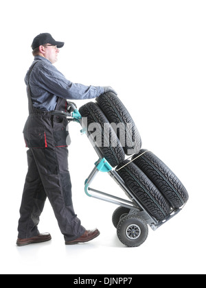 Serviceman carrying a set of four new car tires using hand truck shot on white Stock Photo