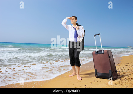 Full length portrait of a lost businessman with his luggage searching for way on a beach Stock Photo