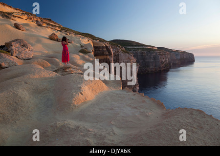 A woman taking pictures of the setting sun from atop the seacliffs at the northwesterly coast of Gozo. Stock Photo