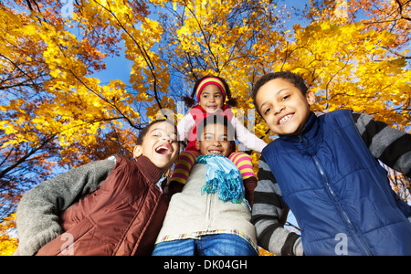 Four black kids, boys and girl, siblings, brothers and sister, smiling, laughing and looking down standing in autumn park Stock Photo