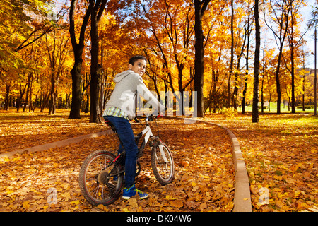 Nice black boy riding a bicycle in the autumn park full of autumn leaves turning back Stock Photo