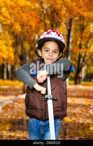 5 years old black boy wearing helmet riding scooter in the autumn park wearing helmet Stock Photo