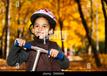 Close portrait of 5 years old black boy wearing helmet riding scooter in the autumn Stock Photo