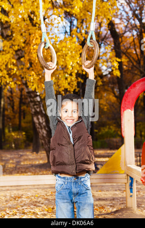 5 years old black boy hanging in on rings on playground in the autumn park Stock Photo