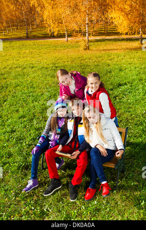 Portrait of five happy kids, boys and girls early teen school age looking in cameras sitting outside with boy holding tablet computer Stock Photo