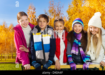 Five happy school age kids, boy and girls, smiling and standing together in autumn park with large happy smiles and stylish looks Stock Photo