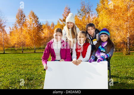 Group of happy teen school age kids in the park with big blank white banner for your text Stock Photo