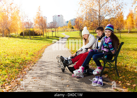 Two girls and a boy putting on roller blades sitting on the bench in the park Stock Photo