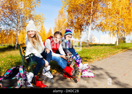 Three happy girls putting on roller blades sitting in the park Stock Photo