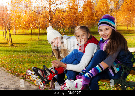 Close portrait of three happy girls putting on roller blades sitting in the park Stock Photo