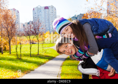 Boy carry girl, both happy and laughing 10 and 11 years old couple of school kids, in warm autumn clothes Stock Photo