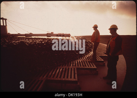 Two workers at a sewage treatment plant during sunset, standing near a rock filter. The image emphasizes the industrial work involved in wastewater treatment and the plant's crucial role in environmental management. Stock Photo