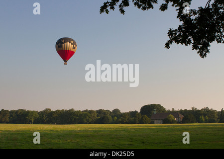 A hot air balloon floats above a church and green field Stock Photo