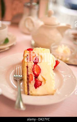 Close up high angle view of slice of strawberry cheesecake on plate next to teapot Stock Photo