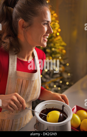 Happy young housewife making apple in chocolate glaze in christmas decorated kitchen Stock Photo