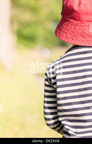 Tranquil summer scene. Young girl with red hat standing outdoors, watching nature. Stock Photo