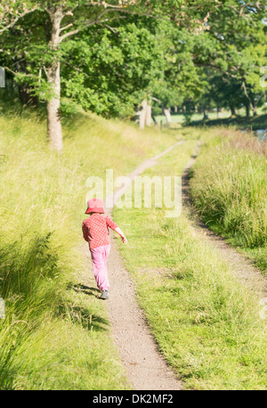 Little girl running on dirt road in green summer landscape, Sweden Stock Photo