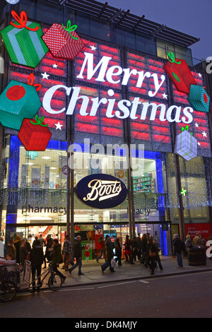 Night street scene shoppers outside shop windows Boots chemist & pharmacy store Oxford Street big Merry Christmas sign in lights London England UK Stock Photo