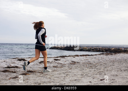 Fit young woman jogger on the beach during her workout. Fitness female model running on seashore. Young woman jogging on beach.