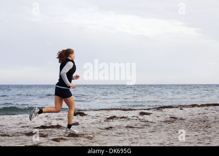 Young female athlete jogging during outdoor workout on beach. Fit and beautiful young woman running. Female runner going outdoor