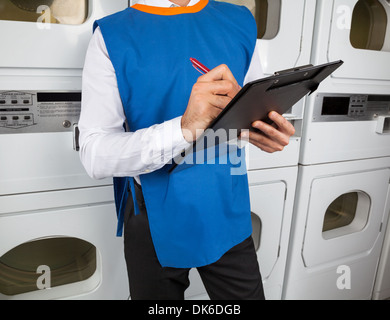 Male Helper Writing On Clipboard In Laundromat Stock Photo