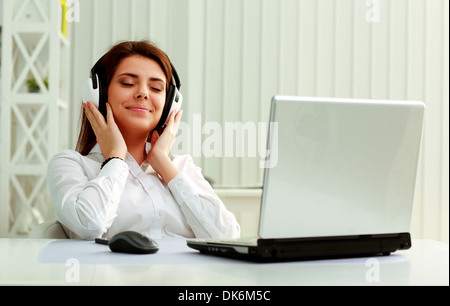Young beautiful businesswoman listening music in headphones at office Stock Photo
