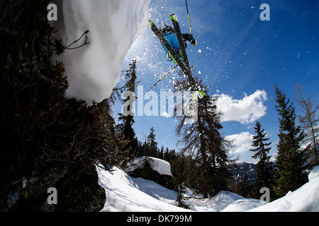 skier jumping from a cliff, photo taken from below with sun and loose snow in the picture Stock Photo