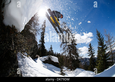 skier jumping from a cliff, photo taken from below with sun and loose snow in the picture Stock Photo