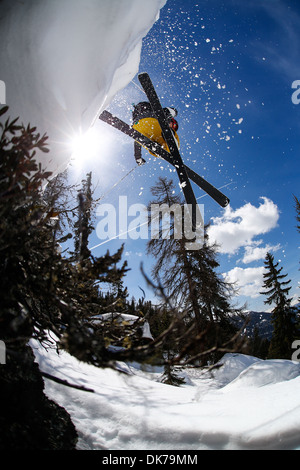skier jumping from a cliff, photo taken from below with sun and loose snow in the picture Stock Photo