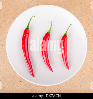 Three fresh raw red hot chili peppers on plate, over light wooden background. Stock Photo