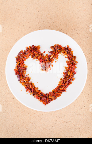 Hot love concept, red chili peppers on plate arranged in heart shape. Stock Photo